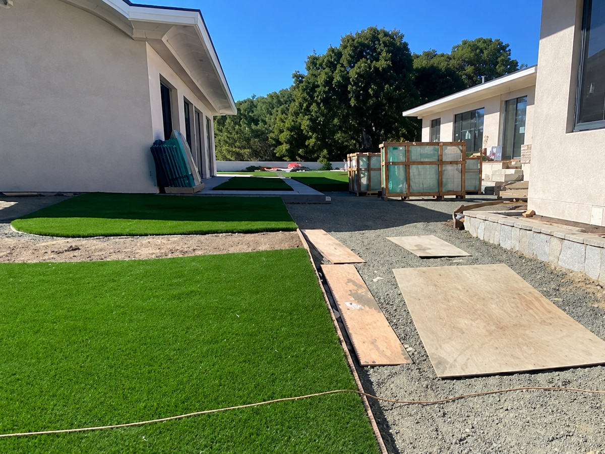 Artificial turf laid beside a gravel path between two light stucco houses