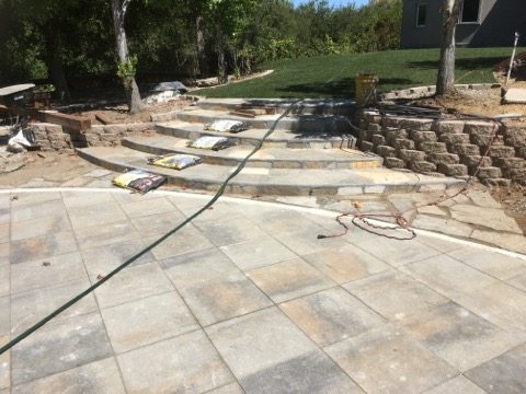 Partly built stone steps and retaining wall beside a new paver patio