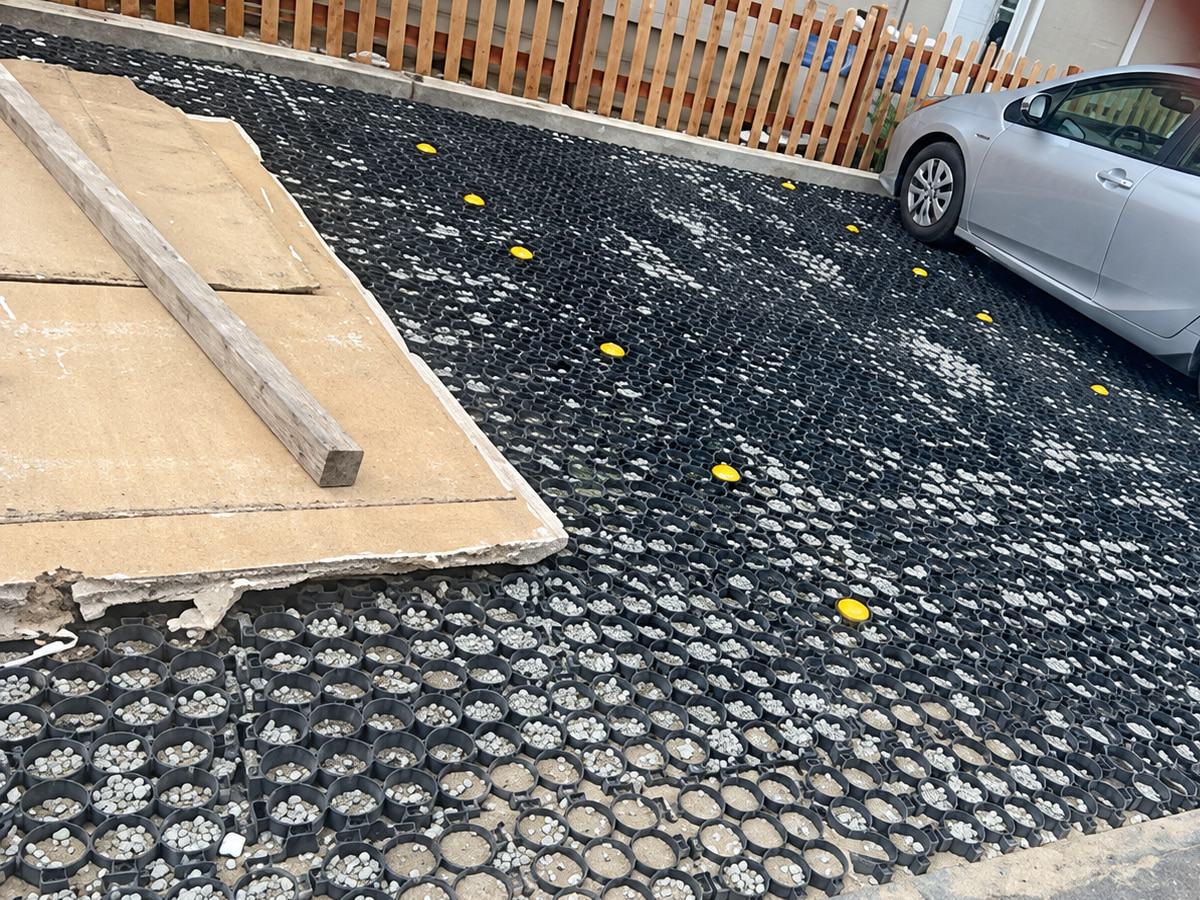 Gravel-filled honeycomb driveway grid going in beside a parked car and wooden fence